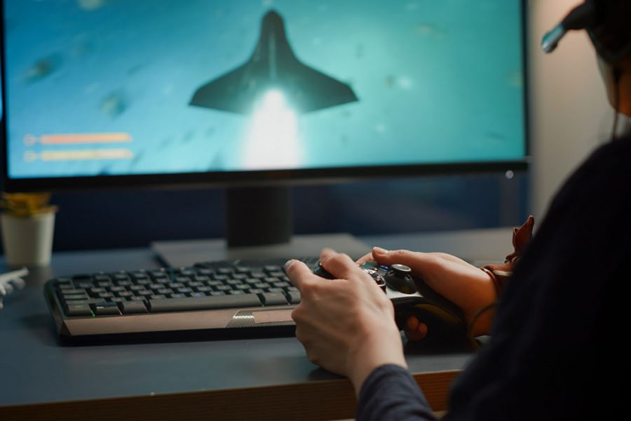 Closeup of competitive woman player holding joystick playing space shooter video games at powerful computer late night. Professional gamer using wireless controller for online gaming championship